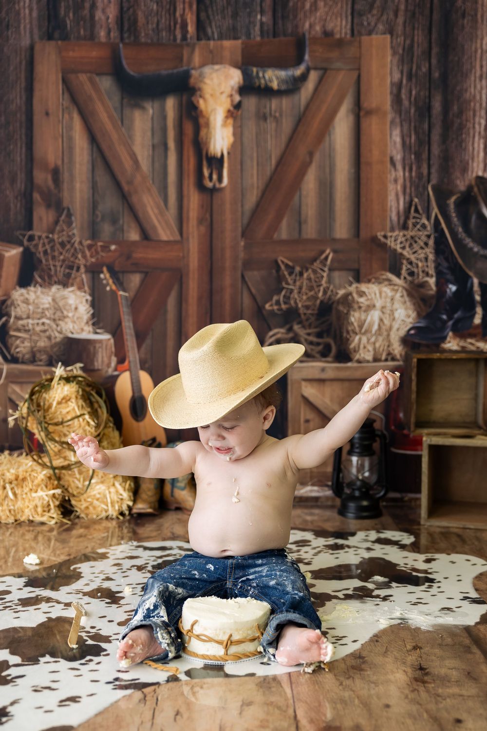 Country western themed photo with yellow cowboy hat, cowhide rug, barn door background and rustic decorations.