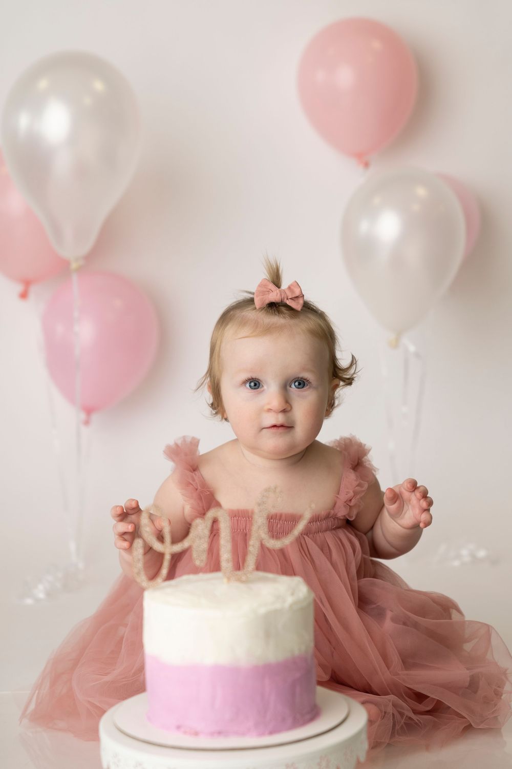 Sweet portrait with pink and white balloons surrounding a small cake with pink and white frosting.