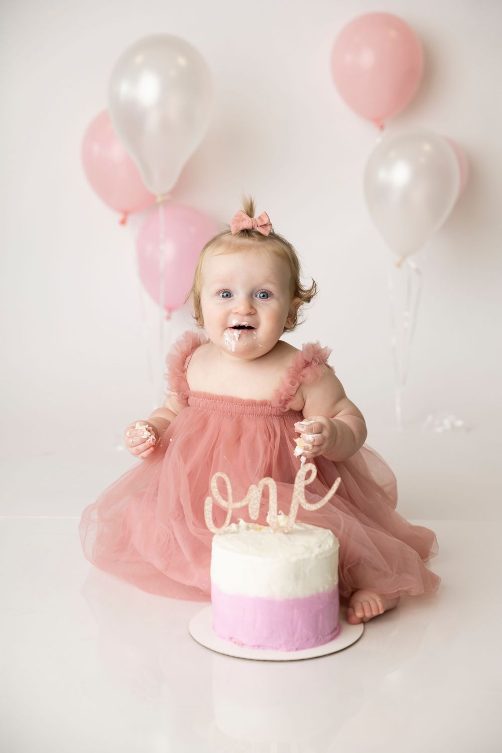Pink and white cake smash photography session with balloons and a baby in a tulle dress.