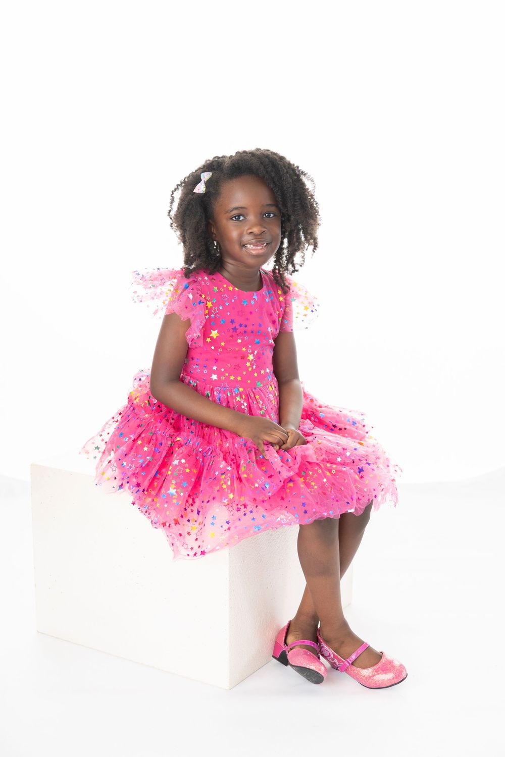 Child in sparkly hot pink tutu dress twirls and poses playfully against white background.