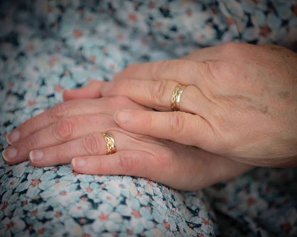 Close-up of two hands wearing matching gold wedding bands resting on a floral dress fabric.