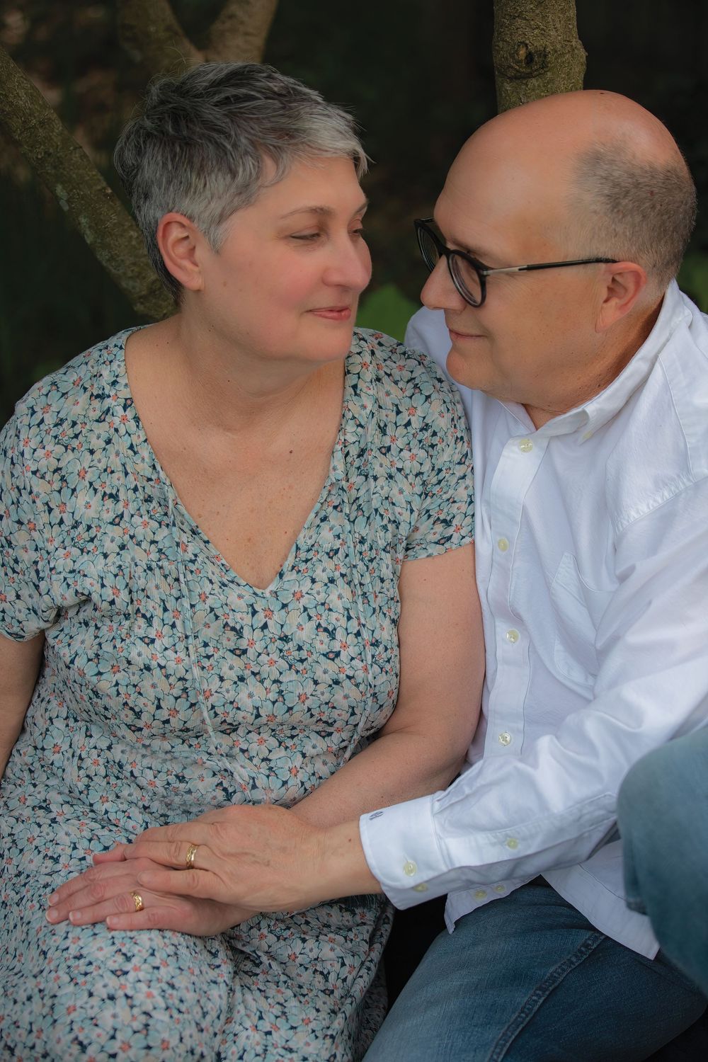 A loving older couple sits beneath a tree, gazing into each other's eyes with gentle affection.