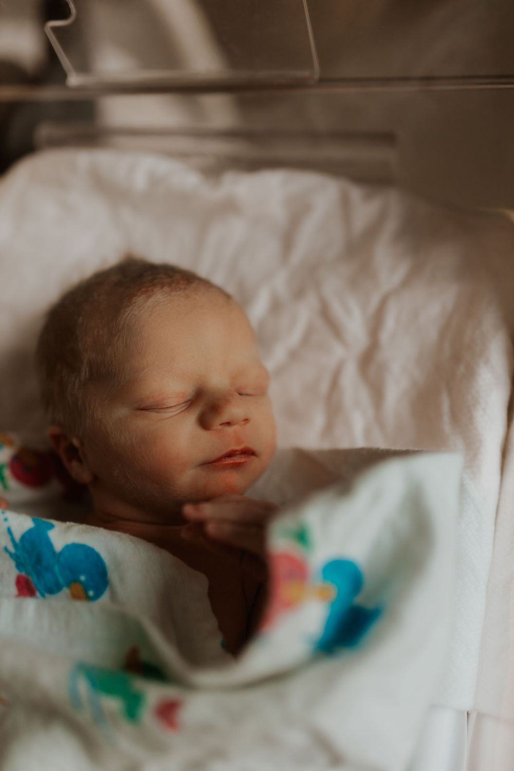 Sleeping newborn wrapped in white blanket with blue and coral pattern details.