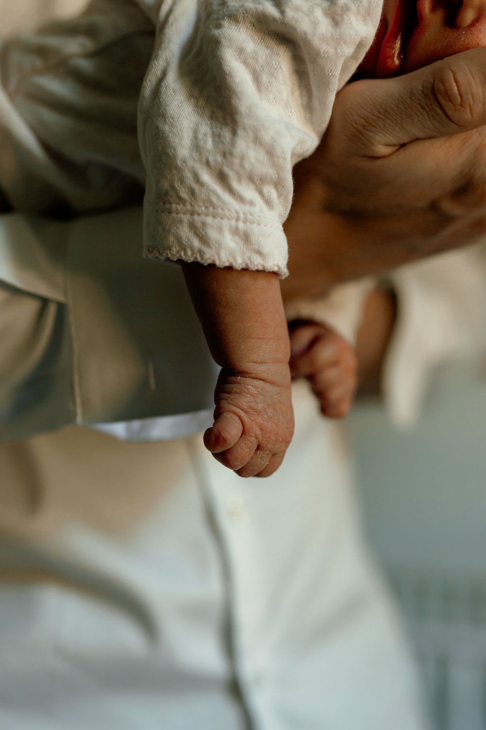 Close-up of a newborn baby's tiny hand and feet resting gently while being held by an adult.