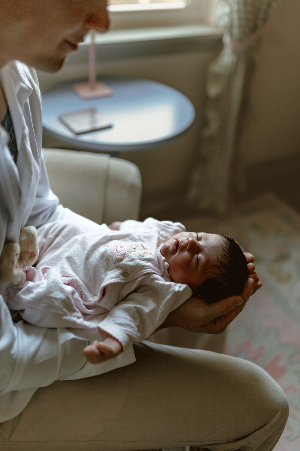 A doctor in a white coat gently holds a sleeping newborn baby in their arms while seated in a chair.