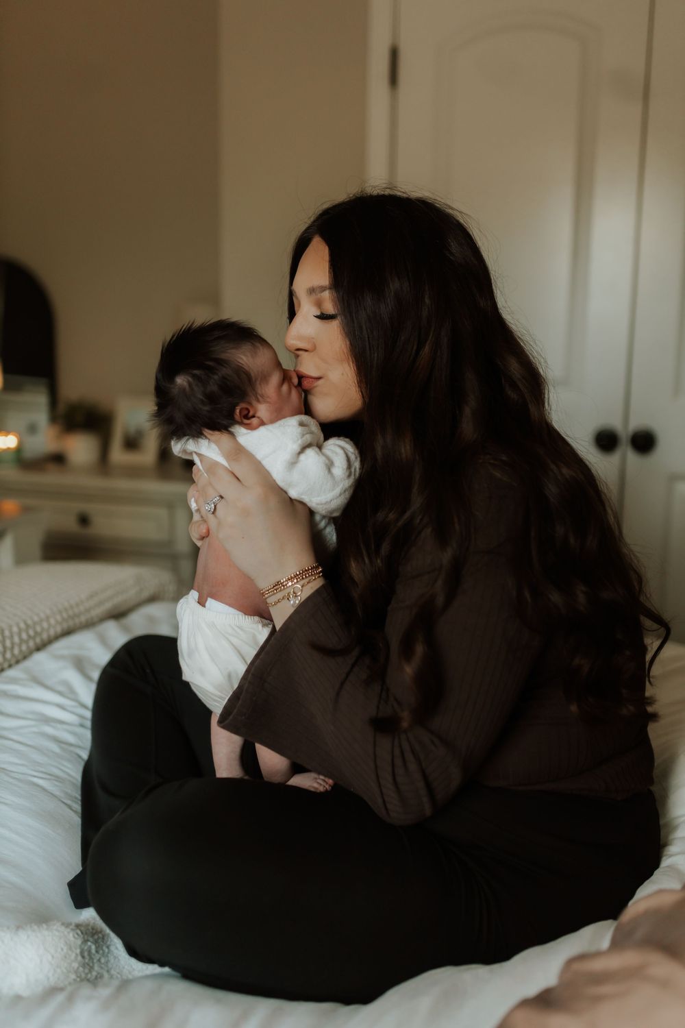 A tender moment captured in soft lighting as a parent holds and kisses a baby in white swaddling clothes on a bed.
