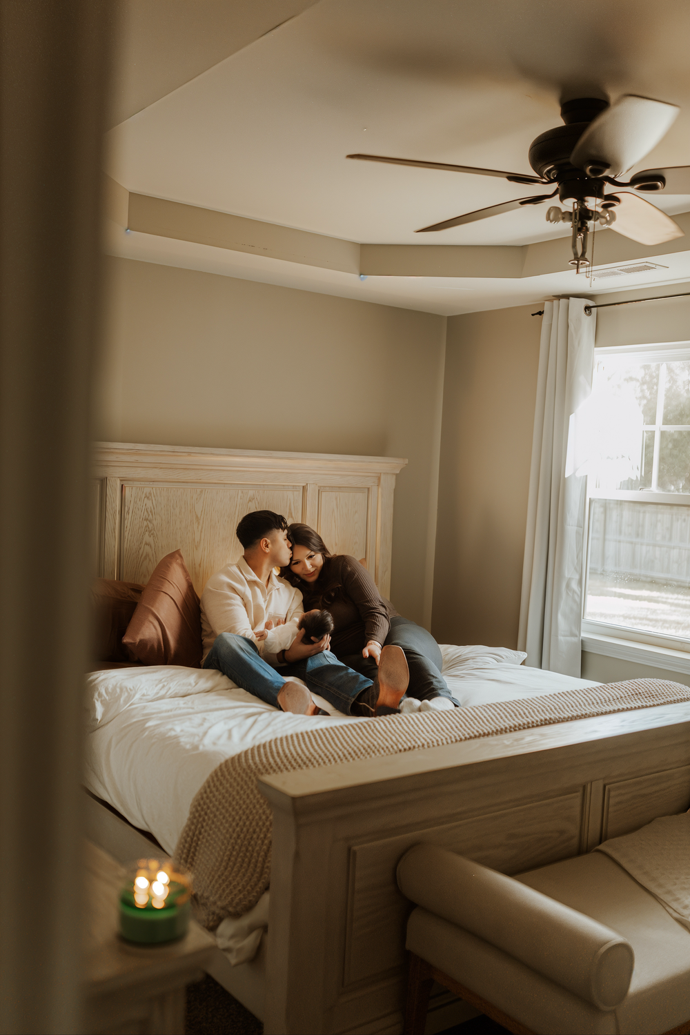 A couple lounges together on a cozy white bed in a minimalist bedroom with natural lighting streaming through windows.