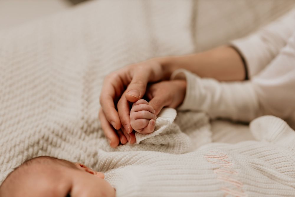 Close-up view of hands gently holding a newborn baby wrapped in soft white blankets.