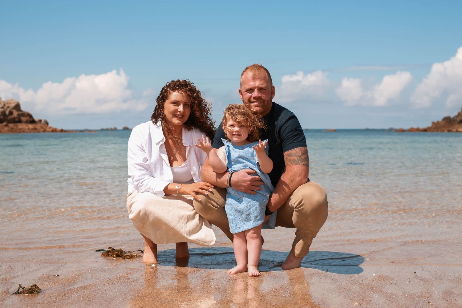 A family poses together on a sunny beach with crystal clear water and blue skies in the background.