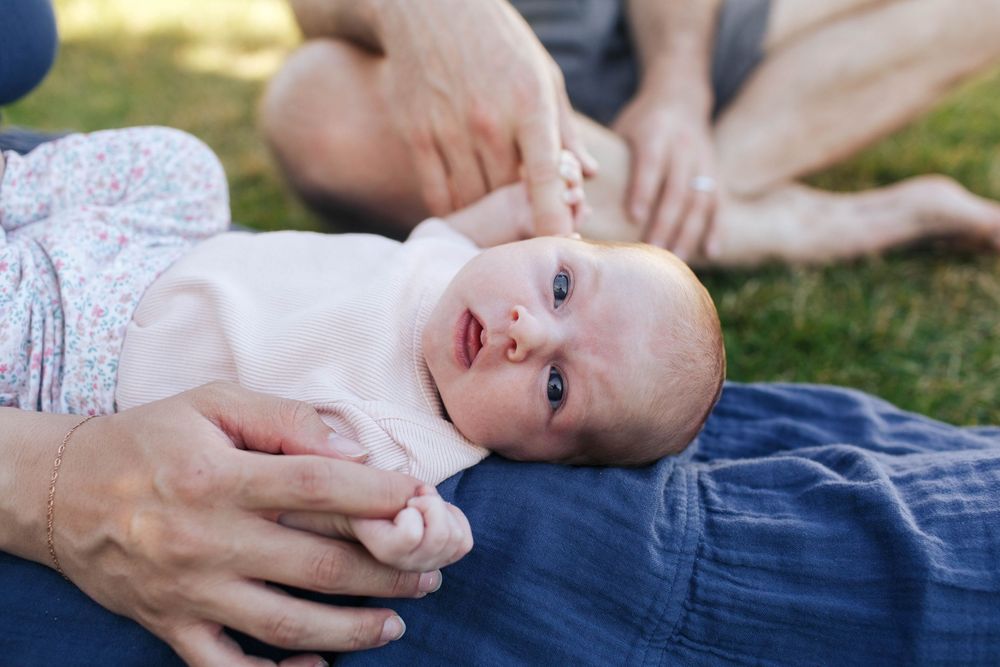 Mukilteo lighthouse newborn photographer: a baby lays on her mother's lap in the grass at the Mukilteo Lighthouse Park in the evening