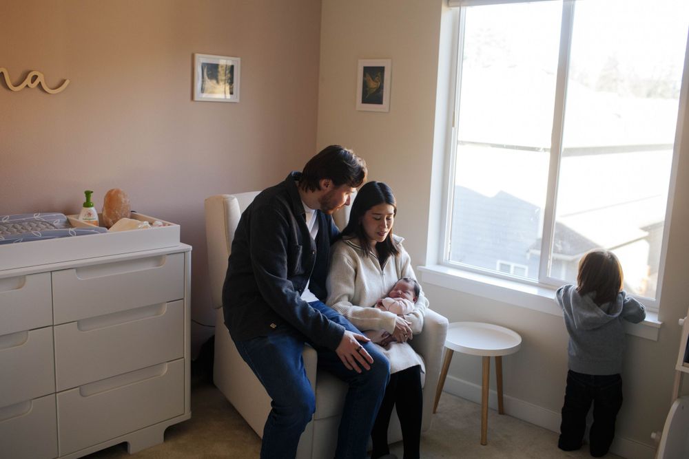 Everett WA baby photographer: a mother and father hold their newborn daughter at a home photo session