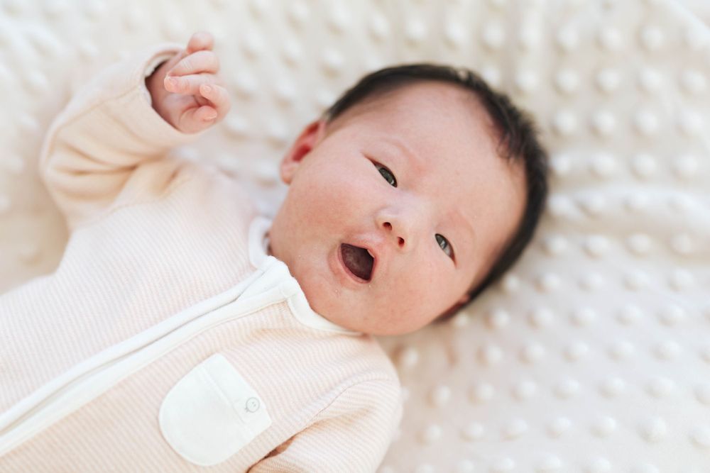 Everett WA newborn photographer: A newborn baby girl gestures to the camera at a home newborn photo session in Everett WA