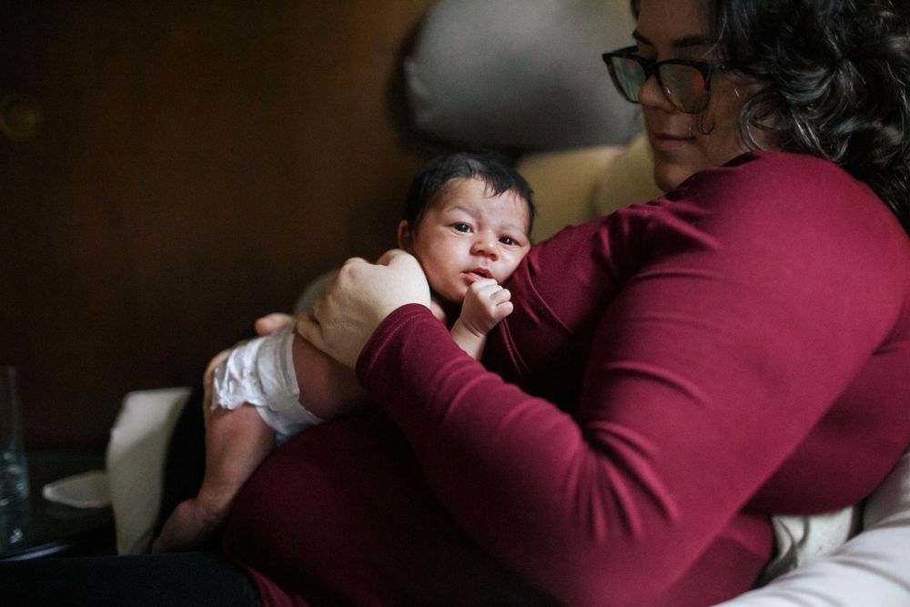 Everett WA newborn photographer: A mother snuggles with her newborn daughter at an in-home newborn photo session in Everett WA