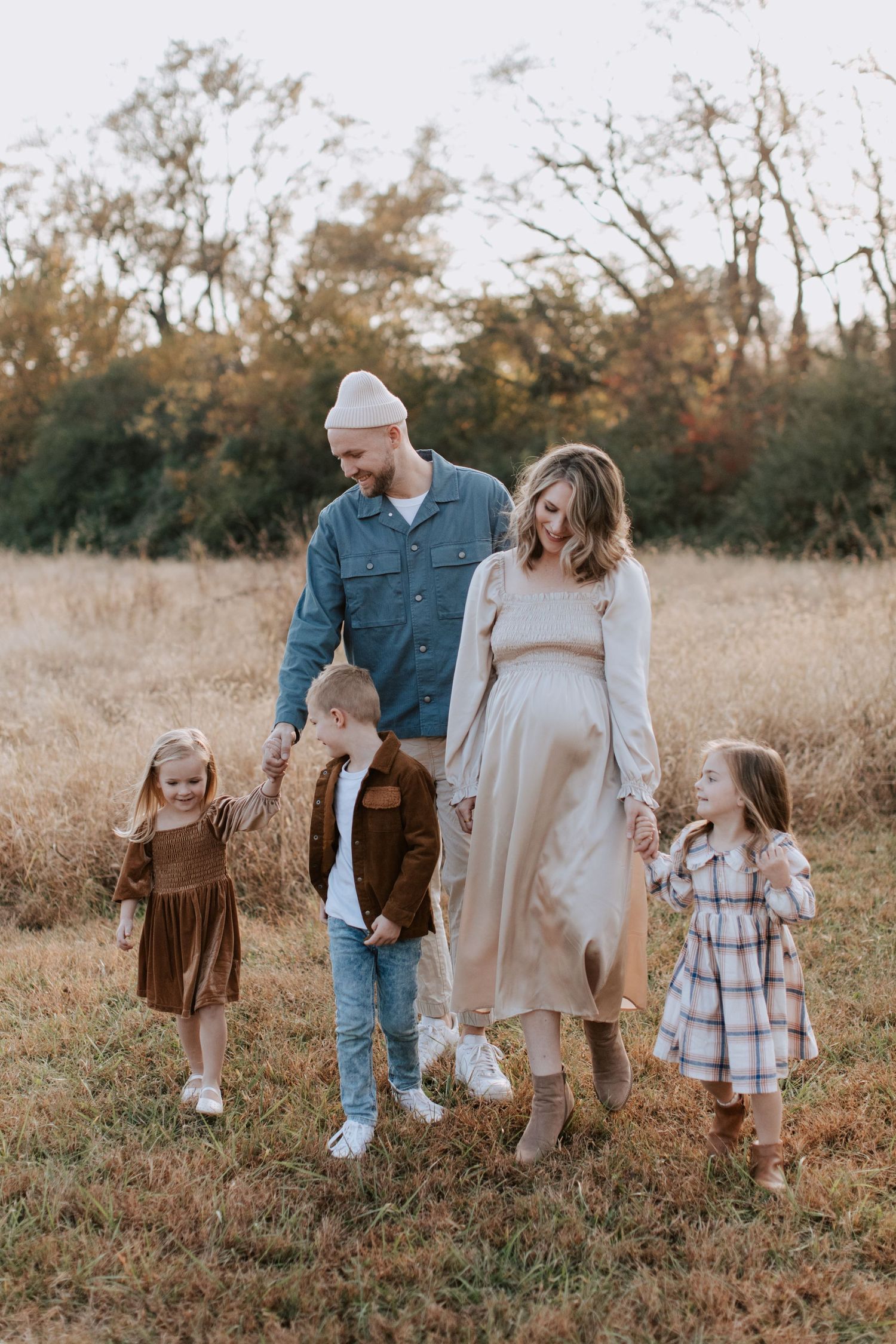Family walking together through autumn field wearing coordinated earth-tone outfits.