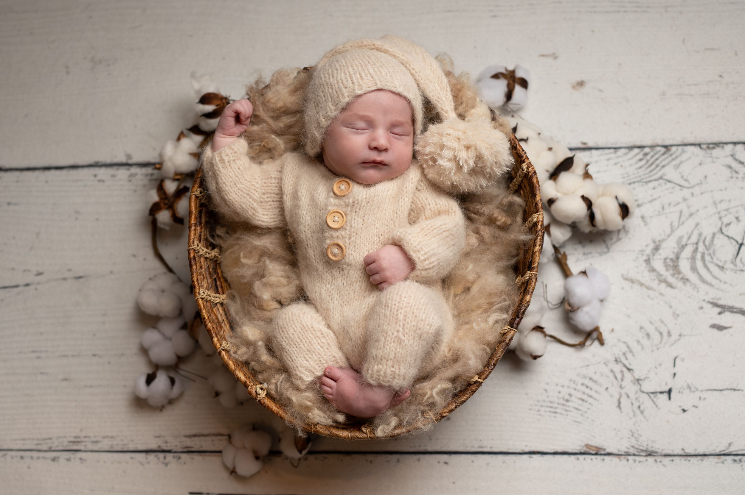 A sleeping newborn baby nestled in a cozy cotton-filled nest with rustic wooden backdrop.