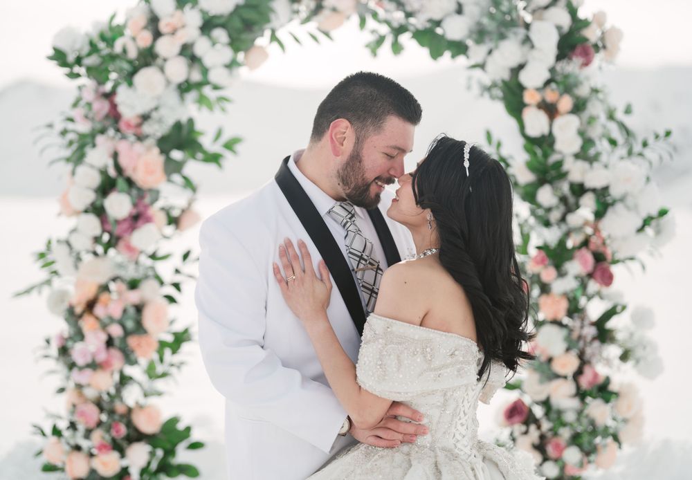 A couple shares a romantic moment under a floral arch decorated with pink and white blooms.