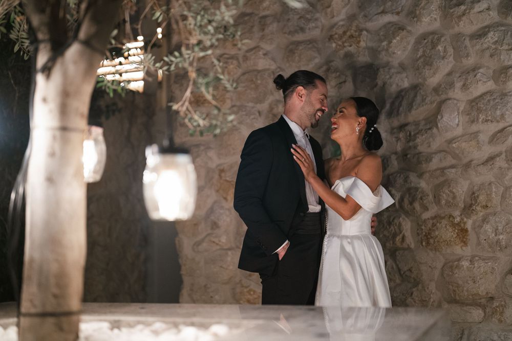 Romantic wedding couple stands close together in stone alcove lit by hanging lanterns creating intimate ambiance.