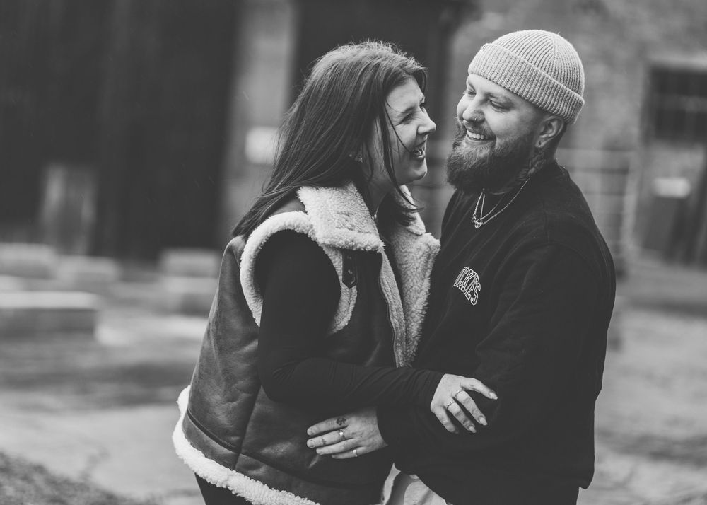 A candid black and white photo shows a couple sharing a sweet moment together outdoors in winter clothing.