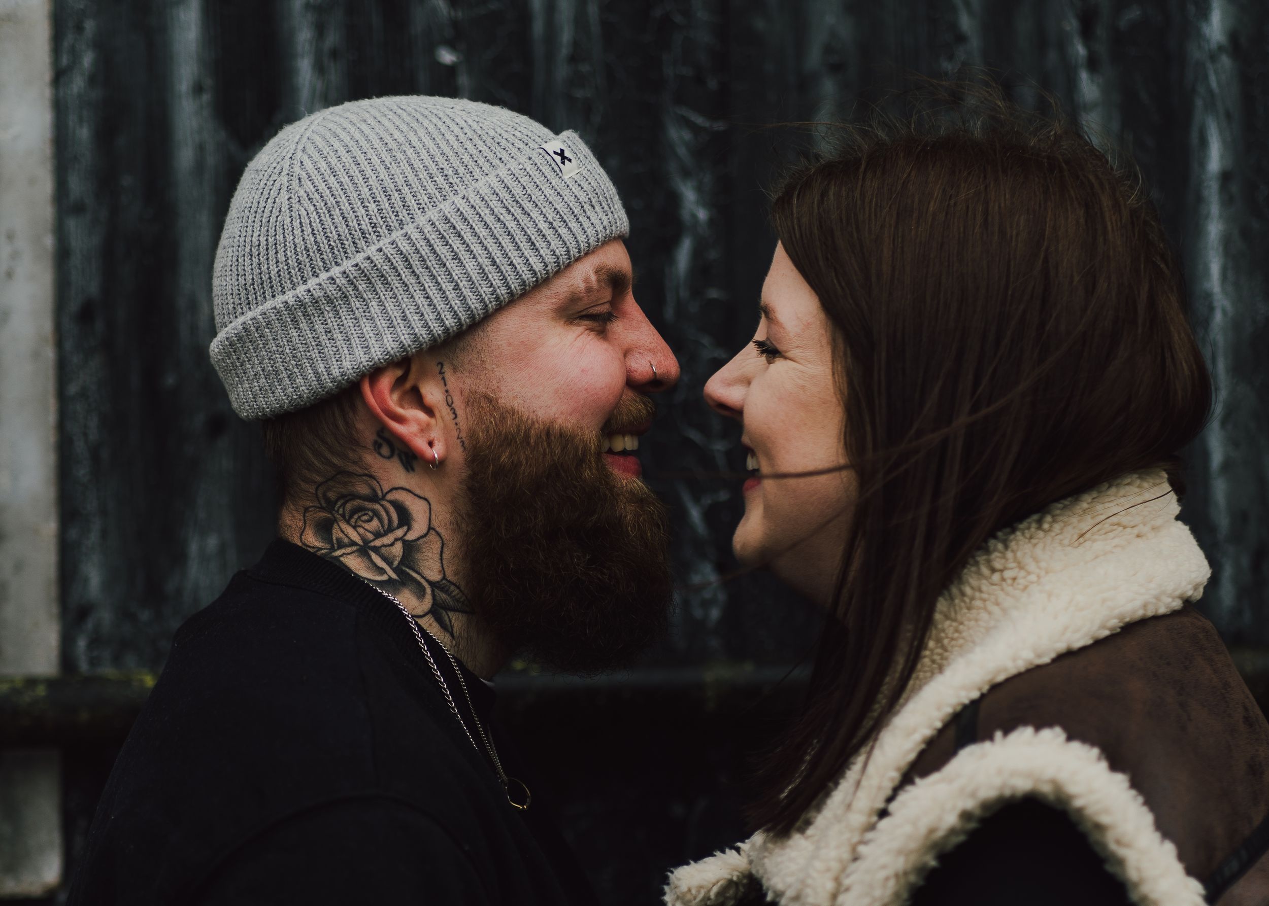 Romantic couple about to kiss in a winter forest scene, with him wearing a beanie and her in a fuzzy coat.