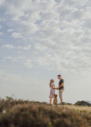 Two silhouettes stand together on a hilltop against a cloudy summer sky during golden hour.