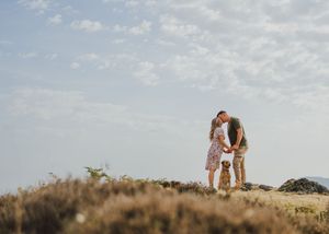 A couple shares an intimate moment while standing on a hill against a cloudy sky during golden hour.
