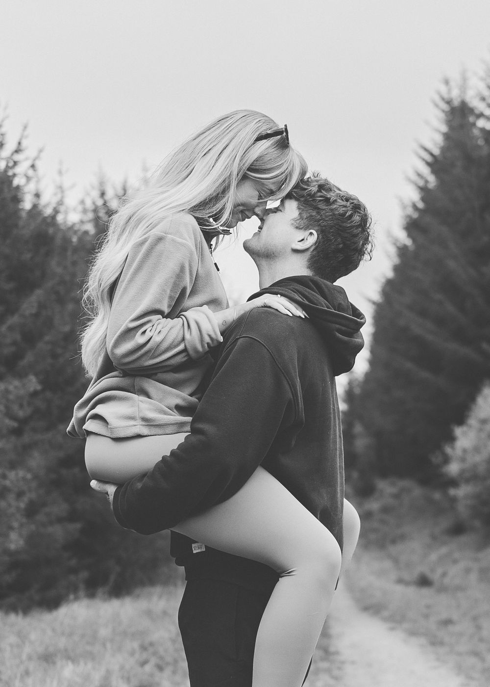 A romantic black and white photo of a couple embracing on a forest path.
