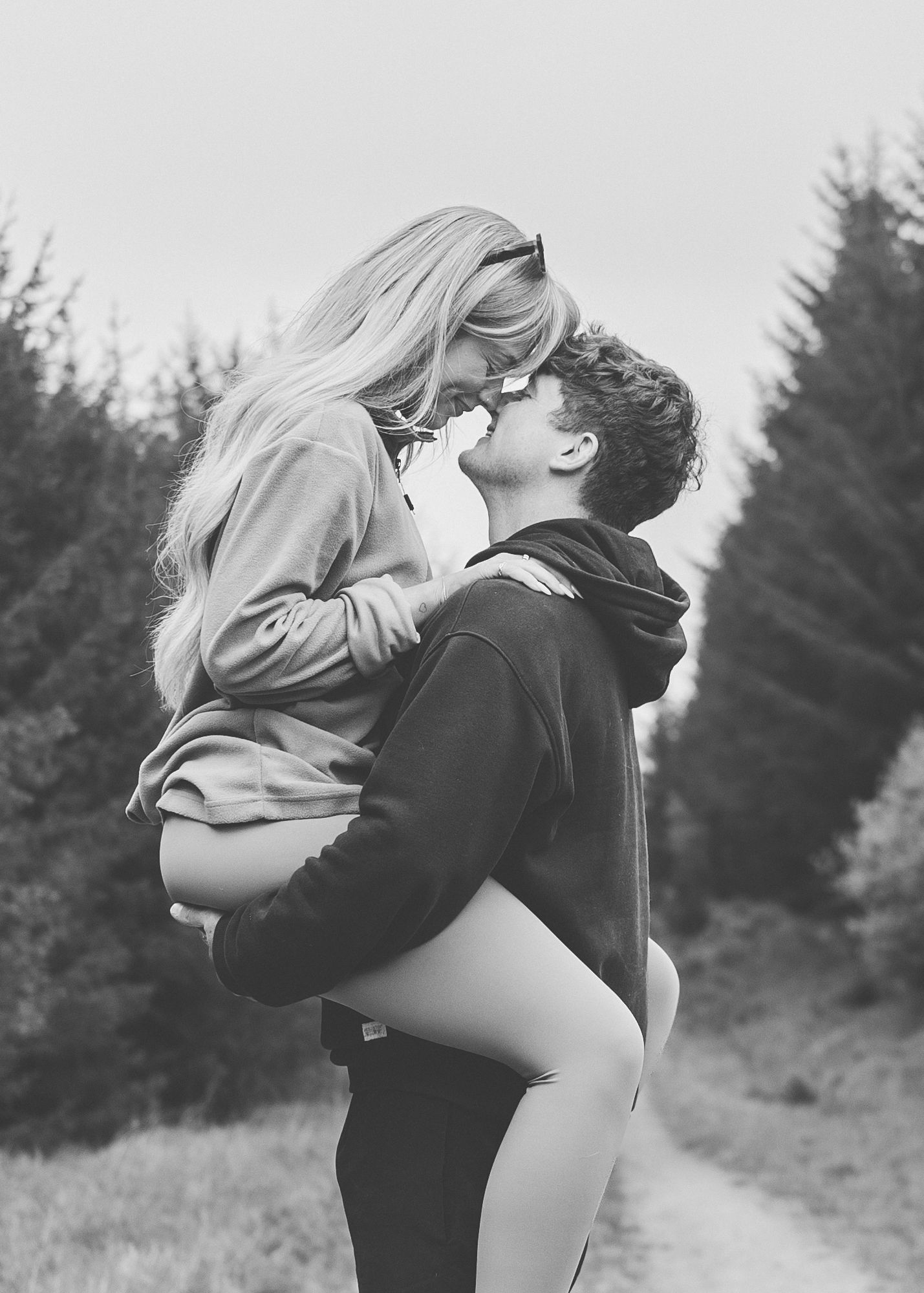 A romantic black and white photo of a couple embracing on a forest path.