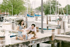 Family of four laughing together on a marina dock surrounded by sailboats on a sunny day.
