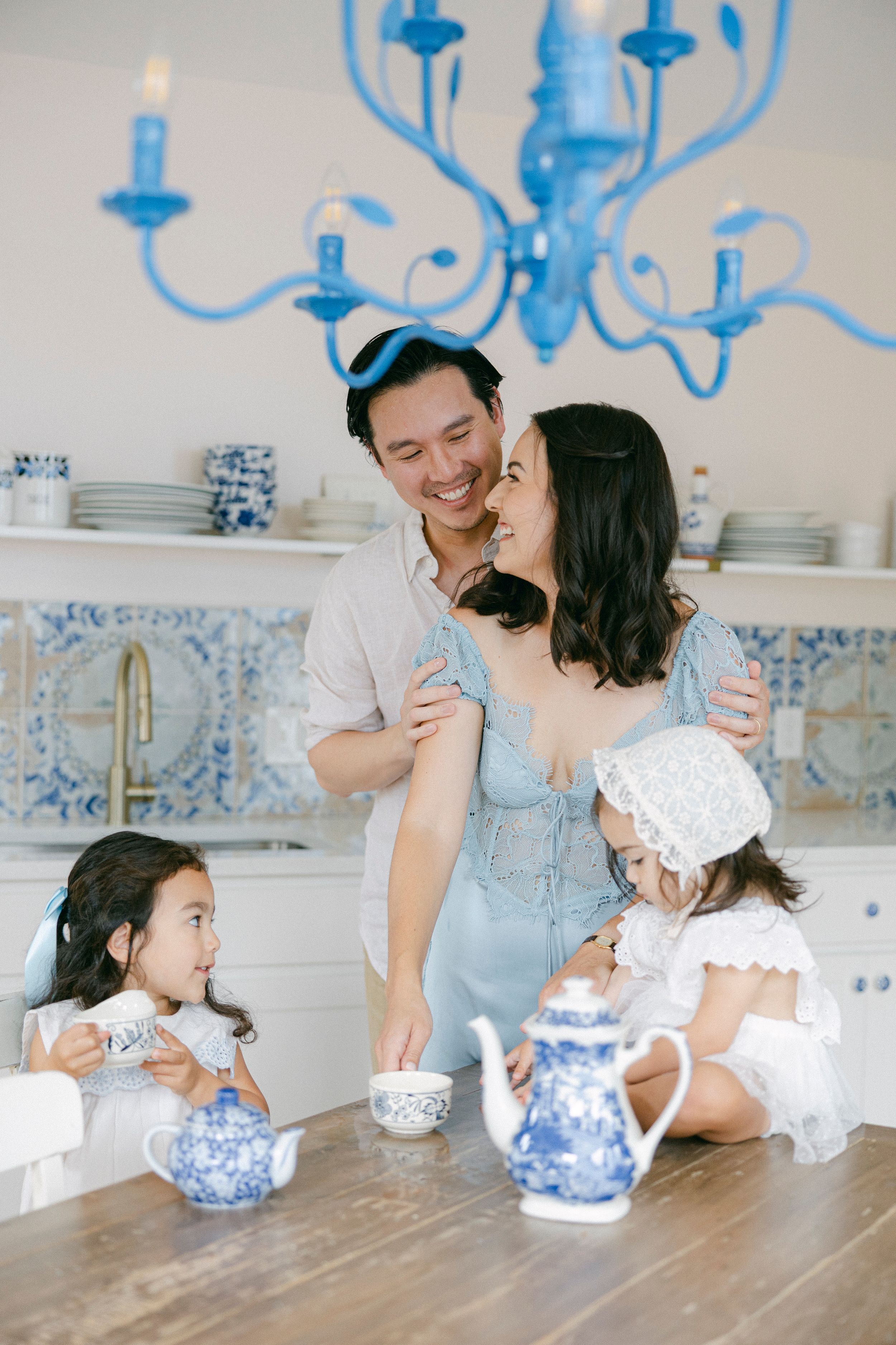 Happy Asian family enjoying a tea party in a bright blue and white kitchen with a chandelier overhead.