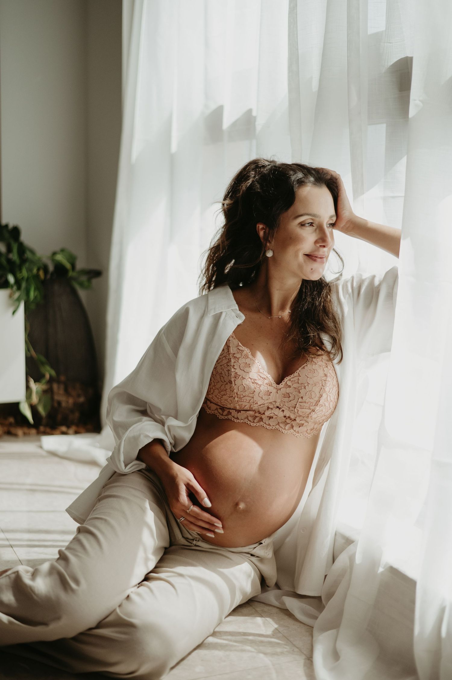 Pregnant woman in white top and jeans smiling while touching her belly in bright room.