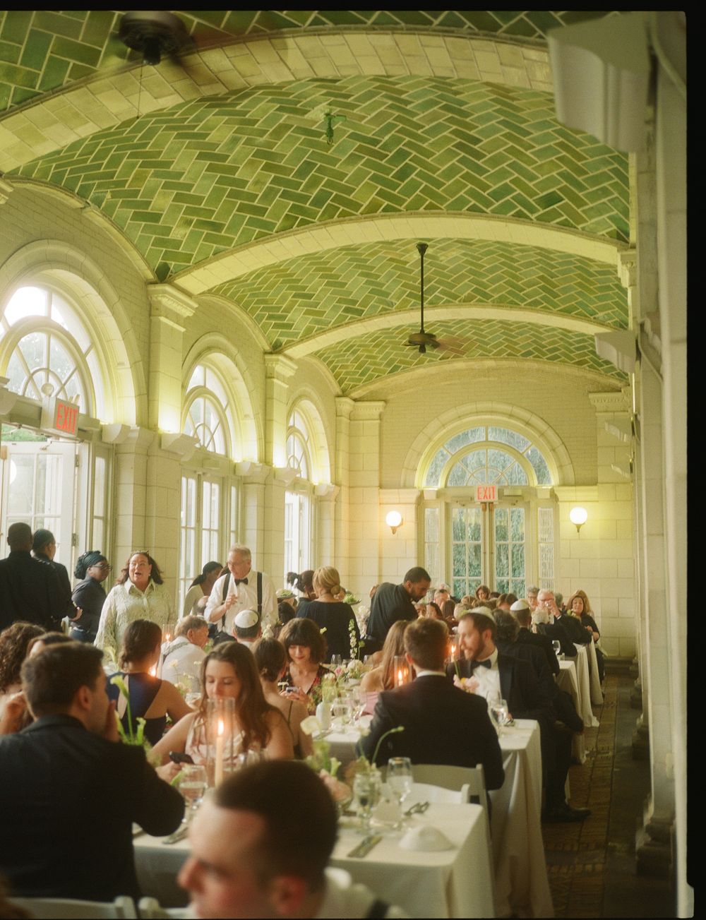 Elegant wedding reception in a grand hall with green herringbone vaulted ceilings, arched windows, and candlelit tables.
