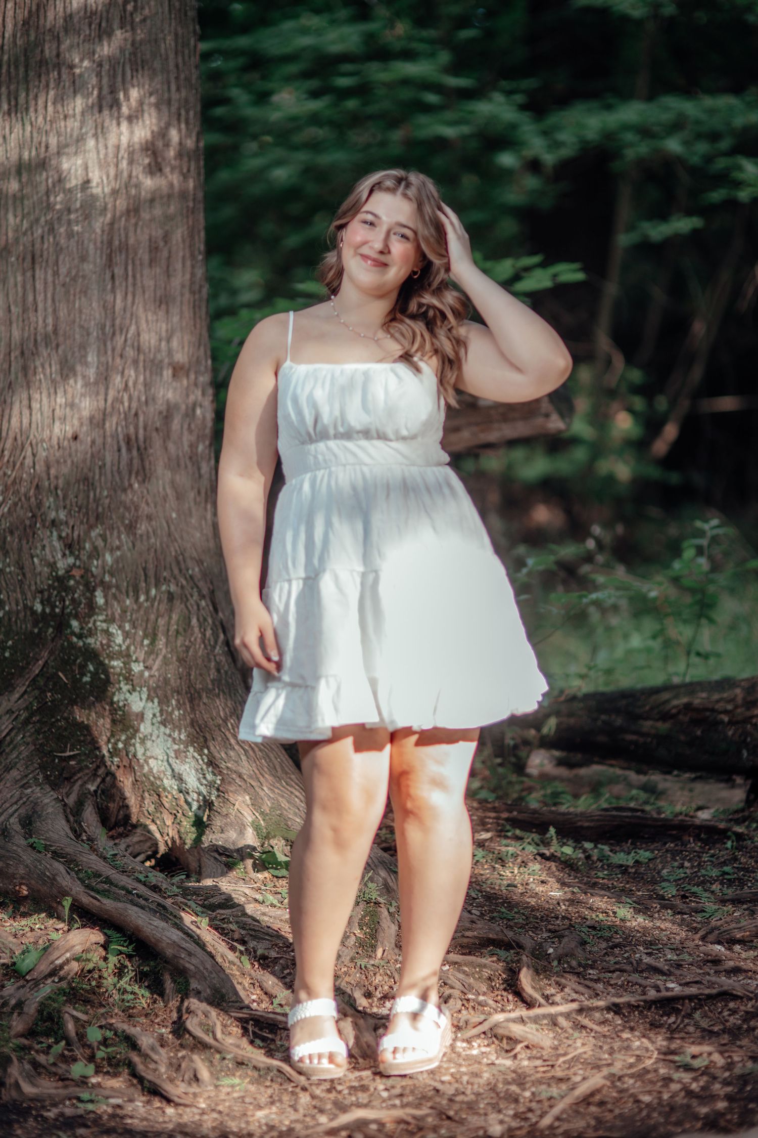 A white sundress catches sunlight in a forest setting with dappled lighting through trees.