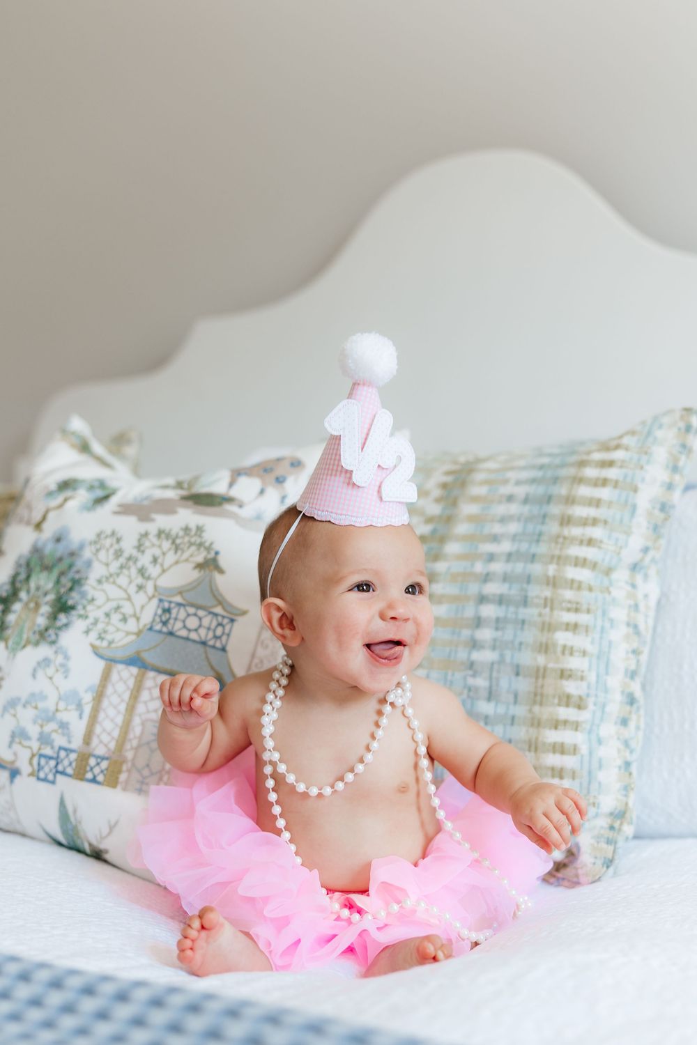 Baby in pink tutu dress and pearl necklace poses on blue and white pillows.