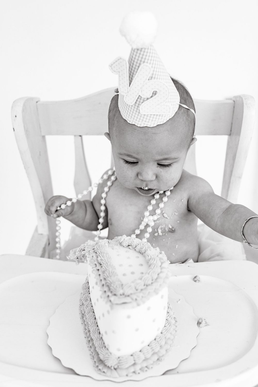Baby wearing white crown and pearls enjoys cake smash photo session.