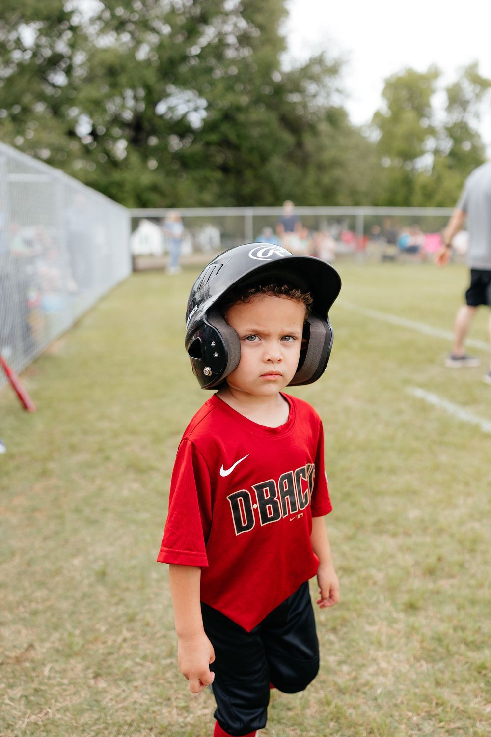 Young boy in red D-backs baseball uniform and batting helmet standing on a youth baseball field.