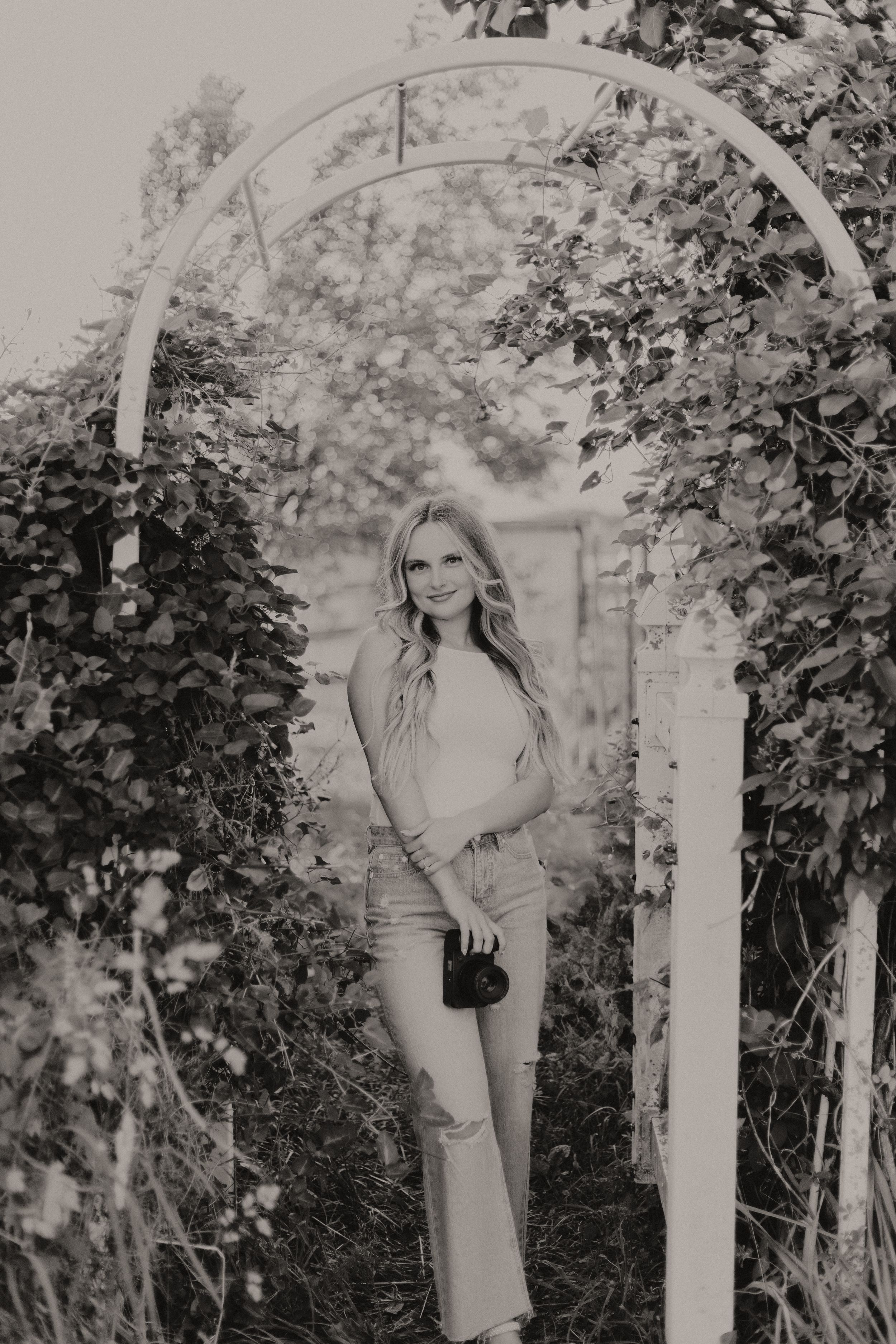 A natural garden arbor covered in vines frames a portrait in black and white photography.