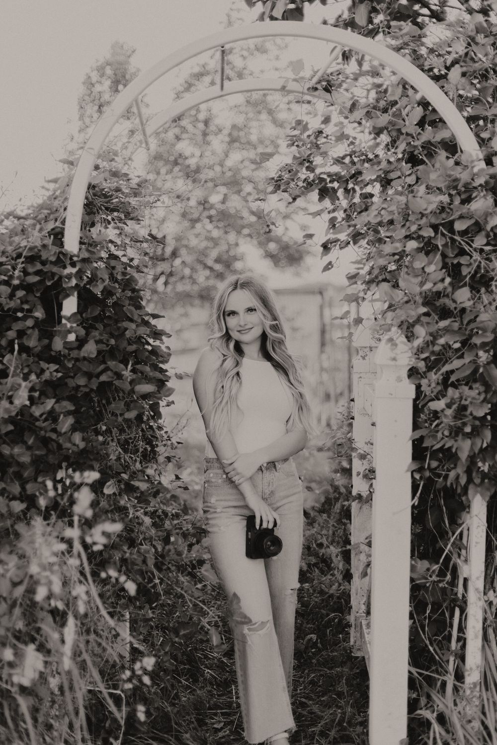 A natural garden arbor covered in vines frames a portrait in black and white photography.