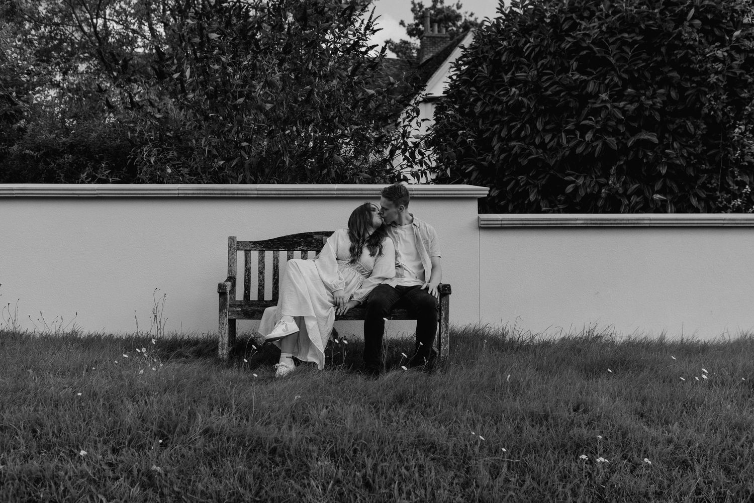 Heterosexual couple kiss privately in wedding venue corridor featuring Italian glass windows and wood panelled walls.