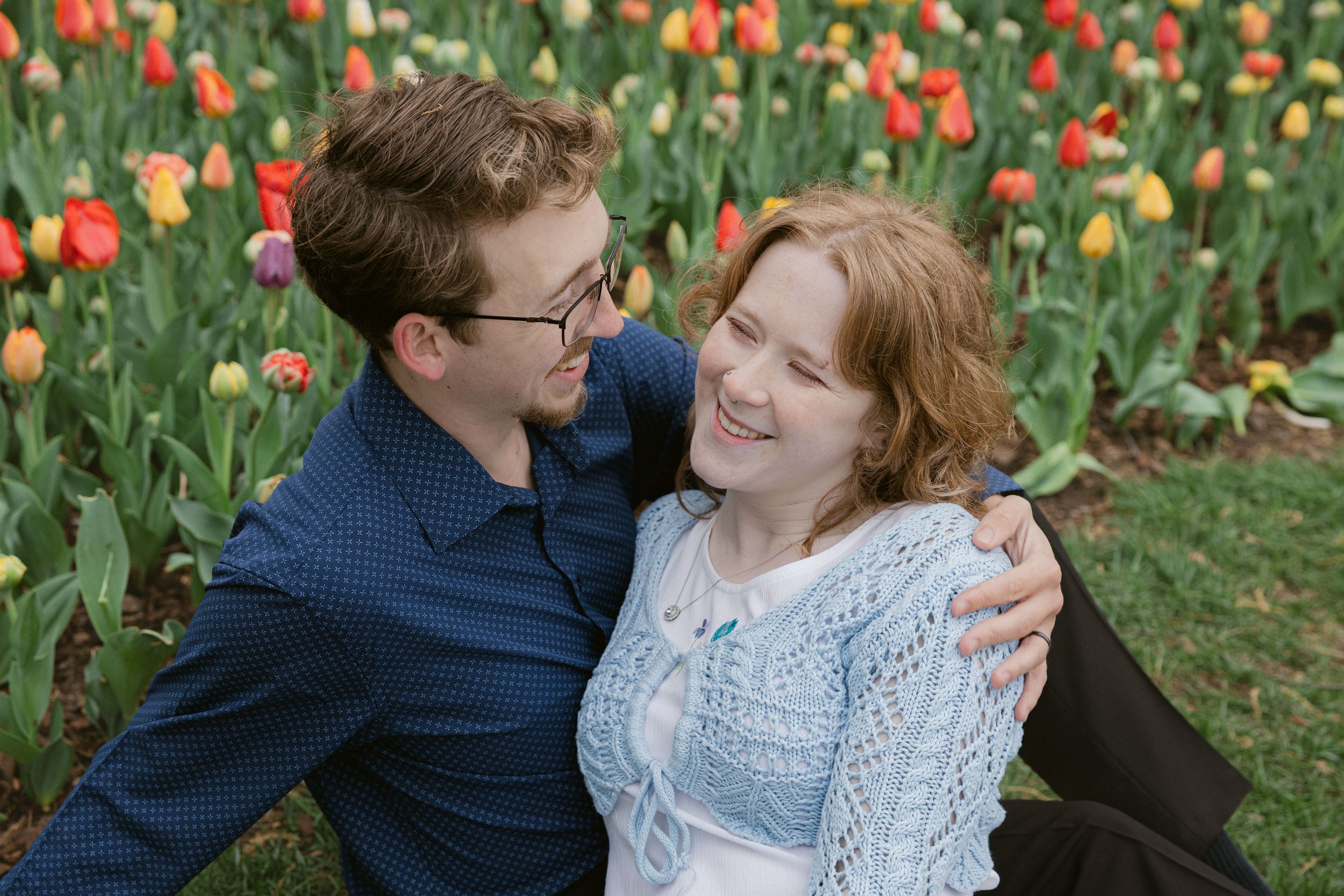 A couple shares a joyful moment together in a vibrant tulip garden during an outdoor photo session.