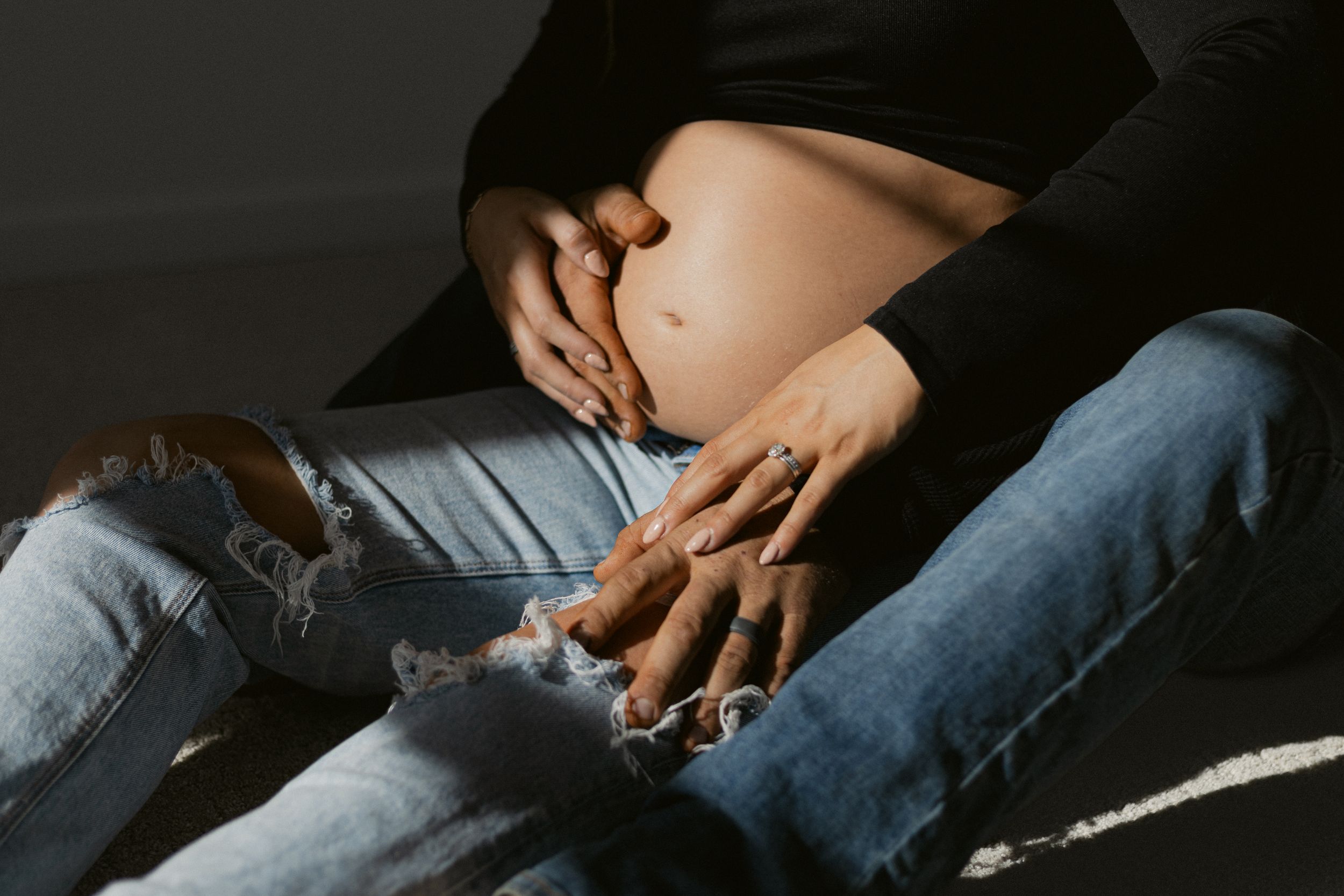 Close-up of hands resting on ripped jeans showing intimate connection.