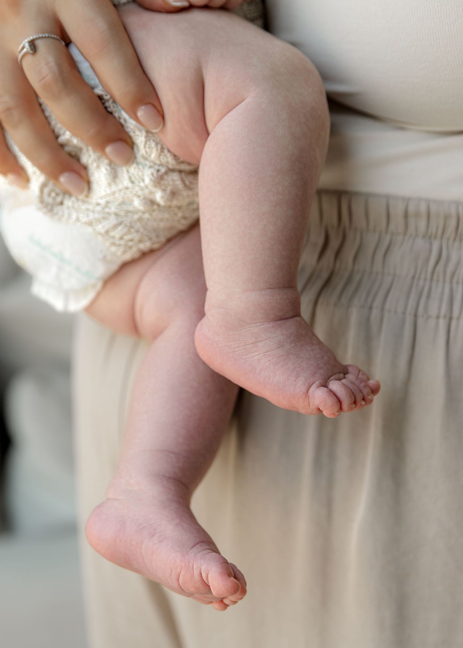 Close up of newborn baby's chunky legs being held by mum - cute baby feet dangling down
