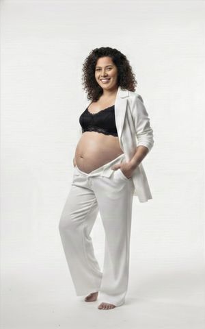 Maternity photoshoot featuring an expectant mother in white pants and black top posing gracefully against white backdrop.