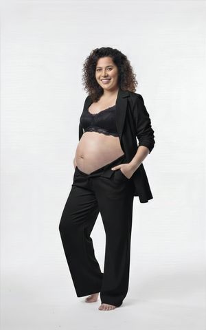 A pregnant woman in black business attire poses confidently against a white backdrop in a maternity photoshoot series.
