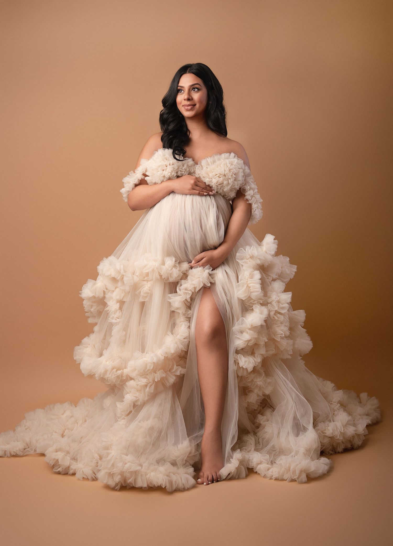 Dramatic portrait session featuring a flowing cream-colored ruffled gown against brown backdrop.