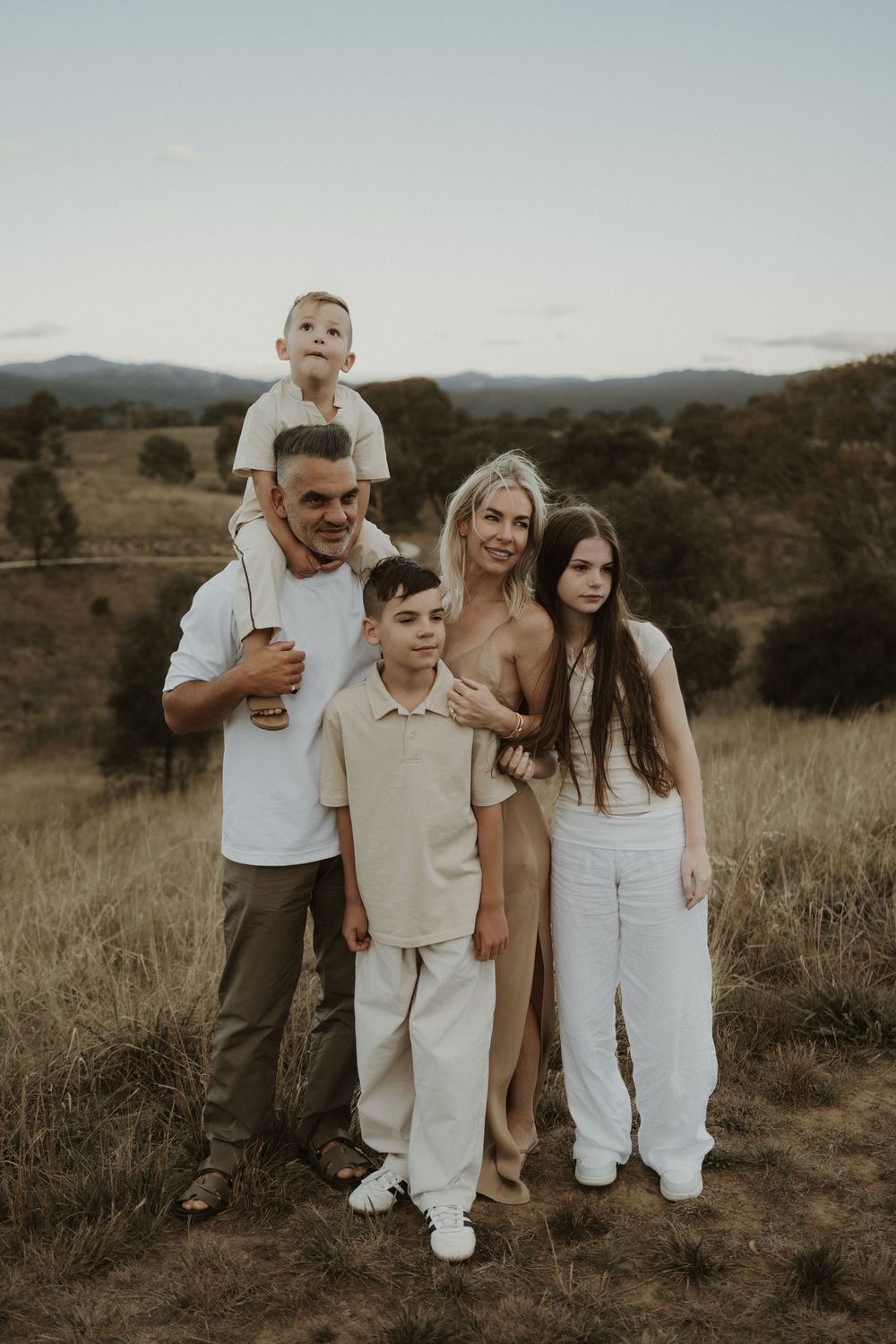 A family poses together in casual attire against a scenic mountain landscape at sunset.