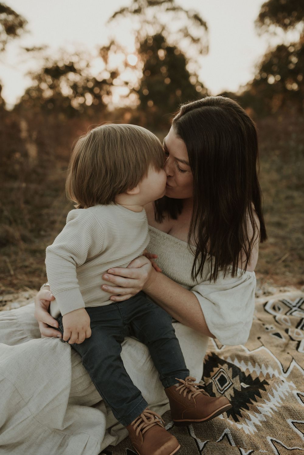 A tender moment between parent and child outdoors at sunset with warm lighting and neutral earth tones.
