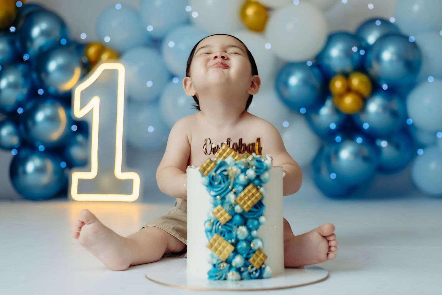 A joyful cake smash photo with green and white balloons and a two-tier birthday cake.