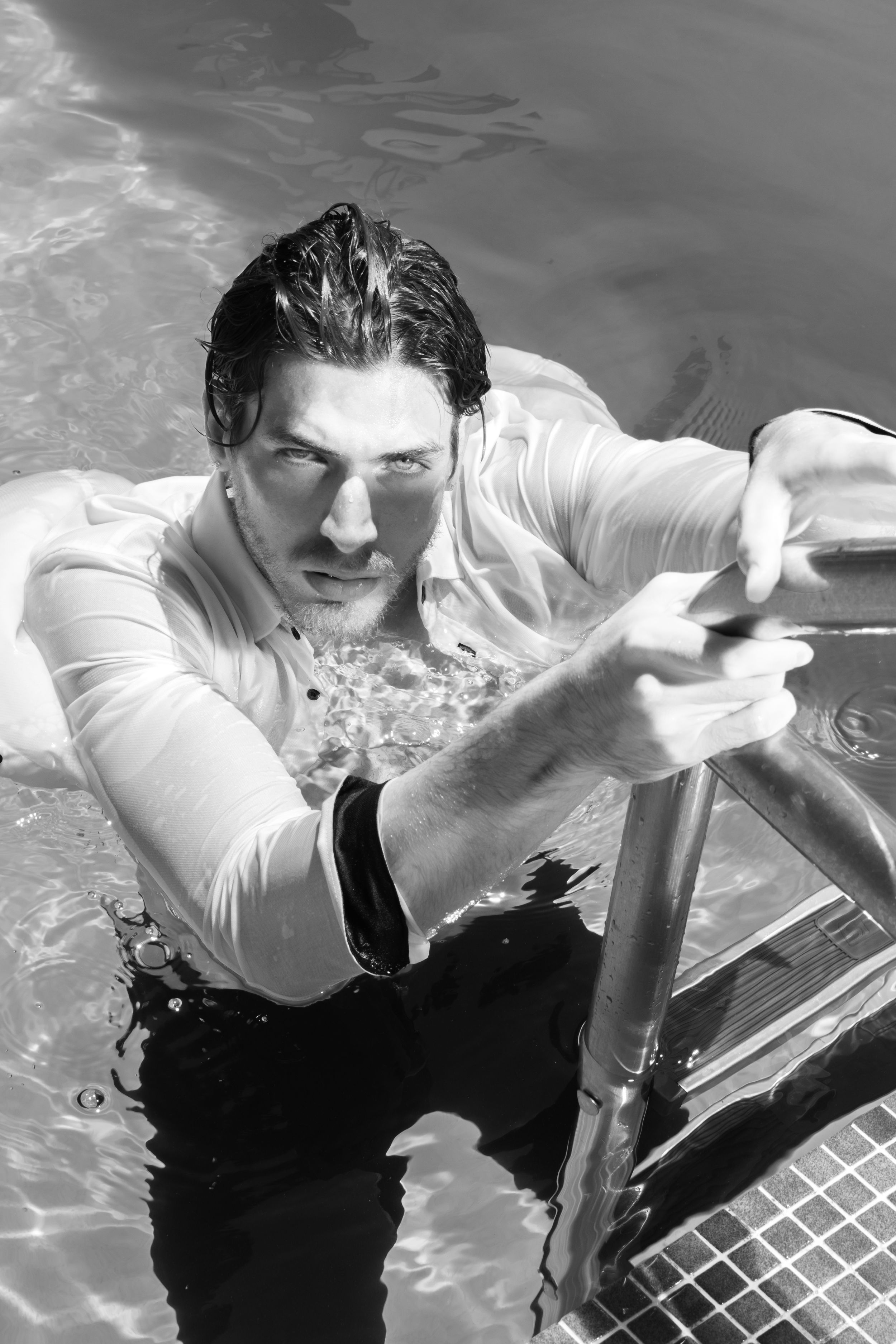 Black and white photo of person emerging from pool water in formal attire.
