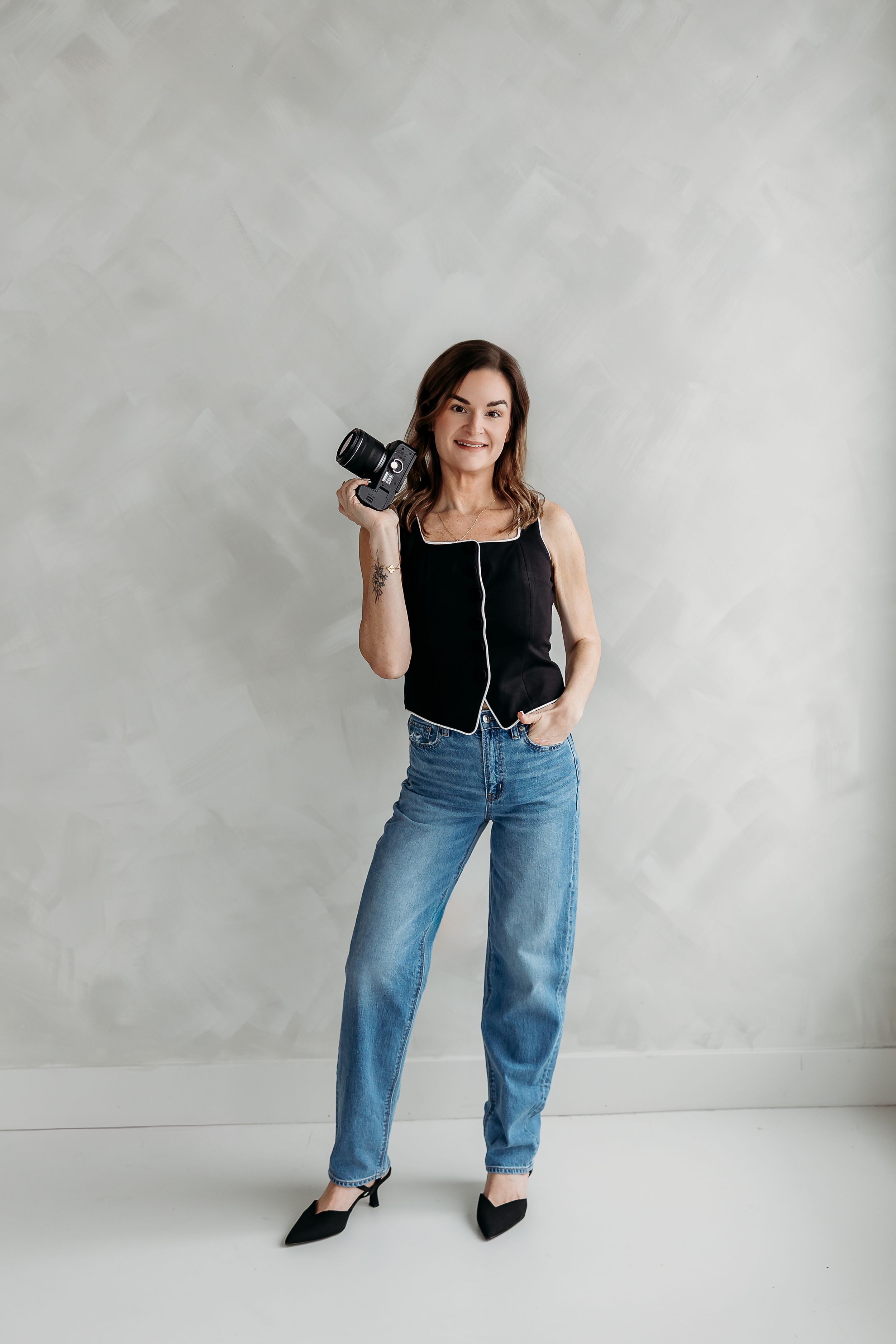Woman in olive green dress and sun hat poses with camera in natural setting.