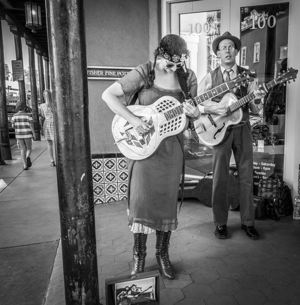 Street musicians perform with acoustic guitars in the square in Santa Fe, New Mexico.   Black and white photography.